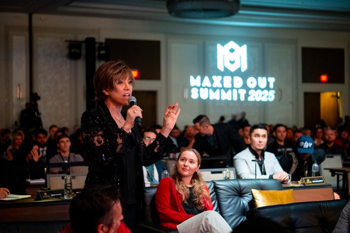 A woman speaking into a microphone among seated conference guests