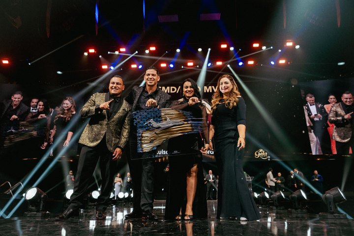 Four guests smiling with an award beneath colorful stage lights