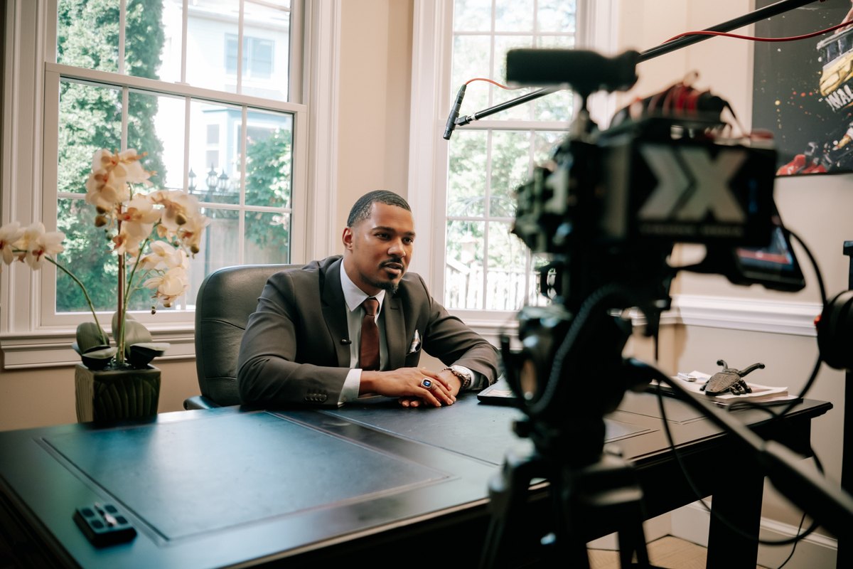 A seated interview guest with a production camera and boom microphone in the foreground