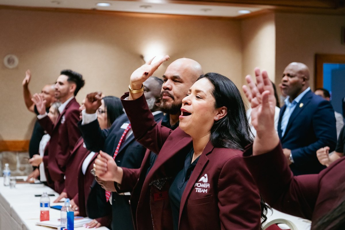 Power Team members in matching burgundy jackets raising their hands during a conference session