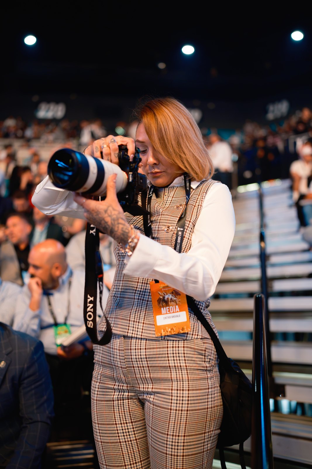 An event photographer looking through her camera in the arena stands